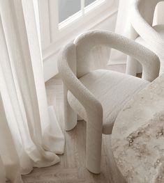 a white chair sitting in front of a window next to a marble table and chairs