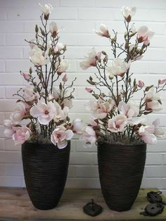 two black vases with flowers in them sitting on a table next to a brick wall