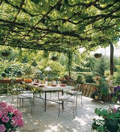 an outdoor dining area with tables and chairs surrounded by trees, flowers and greenery