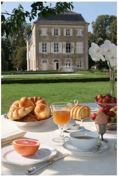 the table is set with food and drinks for two people to enjoy in front of an old house