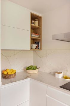 a bowl of fruit is sitting on the counter top in this kitchen with white cabinets