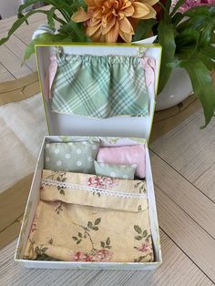 an open box with several folded cloths in it on a table next to a potted plant