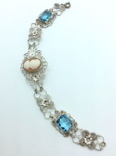 "Work at its best in filagree probably from Spain gorgeous bracelet with a lovely centered cameo and bright blue stone accents Dolly Madison style profile cameo measures 5/8 by 1/2 inch. The clasp is a spring ring style. The bracelet measures 7 .5  long 1\" Wide at center. Gift box with purchase." Formal Blue Bracelets With Cabochon, Blue Cameo Jewelry For Wedding, Victorian Blue Cameo Jewelry, Blue Intricate Design Jewelry Bracelet, Antique Blue Bracelet Jewelry, Elegant Silver Bracelet With Cameo, Elegant Blue Bracelet With Intricate Design, Elegant Blue Bracelets With Intricate Design, Blue Cameo Jewelry For Formal Occasions