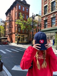 a woman covering her face while standing on the side of a road with buildings in the background