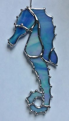 a blue sea horse is hanging from a silver hook on a white background with the word seahorse written below it