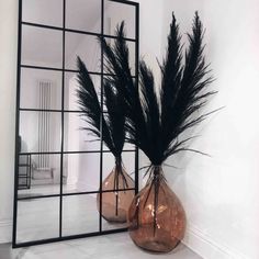 two vases filled with black feathers sitting on top of a white floor next to a mirror