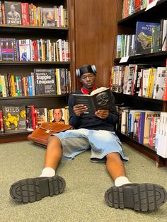 a man sitting on the floor reading a book in front of a library full of books