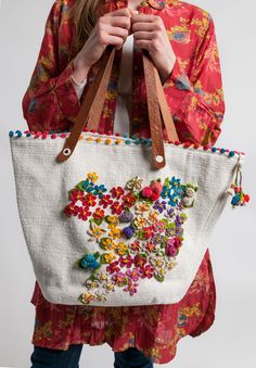 a woman holding a white bag with colorful flowers on the front and bottom, while wearing blue jeans