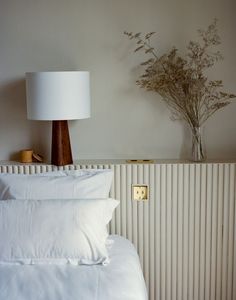 a bed with white sheets and pillows next to a lamp