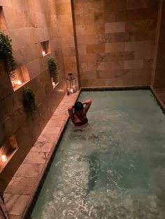 a woman is in the middle of an indoor swimming pool with candles on the wall