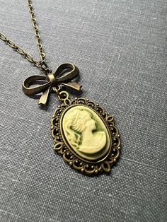 Victorian Lady Cameo Necklace, Charming Sweet Vintage Inspired Necklace, Victorian Gothic Jewelry, Vintage Wedding Gift, Bridesmaid Gift, Vintage Inspired Jewelry  This is a sweet Victorian cameo lady necklace dangling from a cute brass bow of the valley locket necklace and a dainty necklace. This adorable Victorian era style necklace comes in four colors, pick the color that best suits your style, taste, or vintage wedding theme.   This Victorian style necklace is very versatile, it can be a bridesmaid gift, but it can also be an everyday necklace. ❤ Available Colors: Sage Green Cameo Lady Purple/ Lavender Cameo Lady Rose Pink Cameo Lady Olive Green Cameo Lady ❤ Pendant size:  1" Long by 3/4" wide, 1 3/4 inches including the bow Necklace Length: 16 inches- 24 inches  ❤ All items are handm Lady Cameo Necklace, Charming Pendant Necklace For Wedding, Green Vintage Charm Jewelry For Wedding, Green Vintage Charm Jewelry For Weddings, Green Vintage Charm Wedding Jewelry, Vintage Gold Necklaces For Wedding Gift, Victorian Adjustable Necklace For Wedding, Charming Necklaces For Wedding, Charming Handmade Necklaces For Wedding