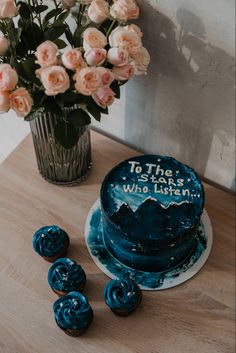 a blue frosted cake sitting on top of a wooden table next to pink roses