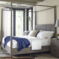 a four poster bed with white sheets and blue throw pillows on the bottom, along with two nightstands