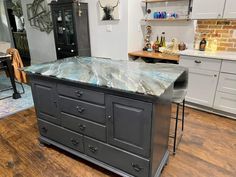 a kitchen island with marble top sitting in the middle of a wooden floored room