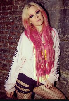 a woman with pink hair and fishnet stockings posing in front of a brick wall