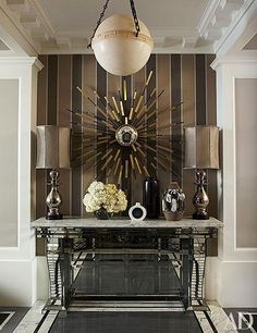 a living room with a table and lamps on top of the fireplace mantel in front of a striped wall