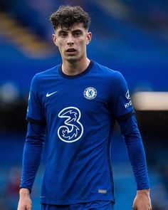 a soccer player is standing on the field with his hands in his pockets and looking at the camera