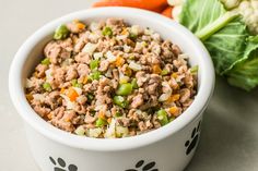 a white bowl filled with food next to lettuce and carrots on a table