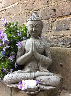 a buddha statue sitting on top of a stone wall next to purple and white flowers