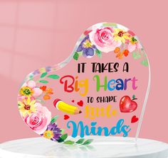 there is a heart shaped sign with flowers and words on the front that says it takes a big heart to shape little minds