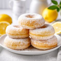 a white plate topped with donuts covered in powdered sugar next to lemons