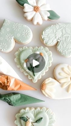 some decorated cookies are laying on a white surface with green leaves and flowers around them