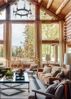 a living room filled with lots of furniture and large windows overlooking the trees in the distance