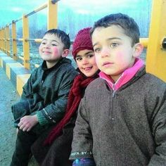 three children are sitting on a yellow bench and one is wearing a red beanie