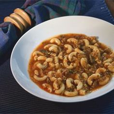 a white bowl filled with pasta and sauce on top of a blue table cloth next to a wooden spoon