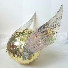 a shiny golden apple with an angel wing on it's side, sitting in front of a white wall