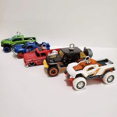 four toy cars lined up in a row on a white surface, with one red and one green