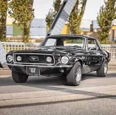 an old muscle car is parked on the side of the road in front of a bridge