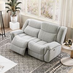 a grey reclining couch sitting on top of a rug in a living room next to a window