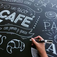 a person writing on a blackboard with white chalk and some type of lettering in the background