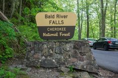 a sign for bald river falls in the woods with cars parked on the road behind it