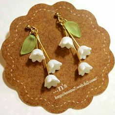 three white flowers with green leaves hang from gold earwires