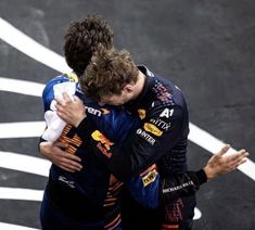 two men hugging each other while standing on top of a race track