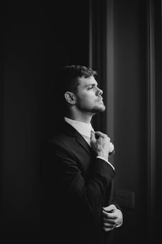 a man adjusting his tie while standing in front of a window, black and white photo