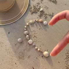 someone is making a heart out of seashells in the sand with their hand