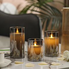 three candles sitting on top of a table next to cups and saucers with flowers