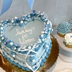 a heart shaped cake sitting on top of a table next to cupcakes with frosting