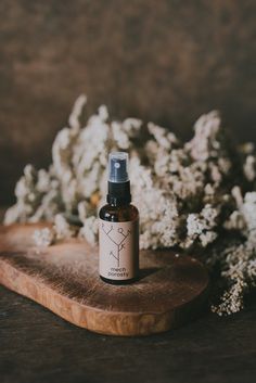 a bottle of essential oil sitting on top of a wooden cutting board next to flowers