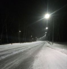 a snowy road at night with street lights in the distance