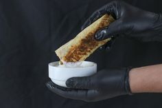 a person in black gloves is dipping food into a small white bowl on a black background