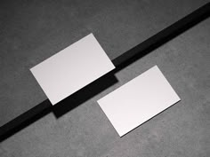 two blank business cards sitting on top of a table next to a black and white pencil