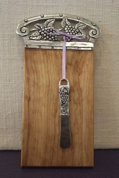 a wooden plaque with a grape design on it and a metal spoon in the middle