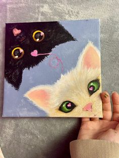 a person holding up a painting with two cats on it's face and one has green eyes