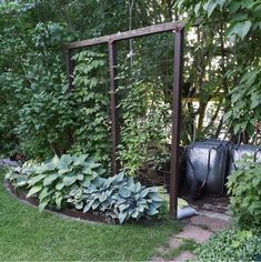 a garden with lots of green plants and trees in the background, along with a black bag on the ground