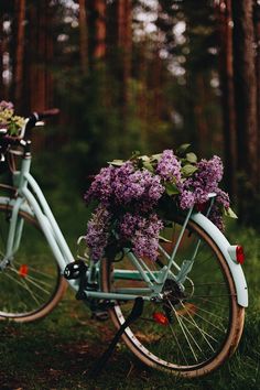 a blue bicycle with flowers in the basket on it's handlebars parked next to some trees