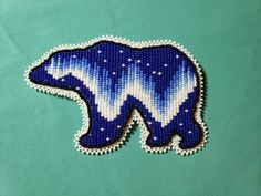 a blue and white beaded polar bear on a green surface with snow flakes